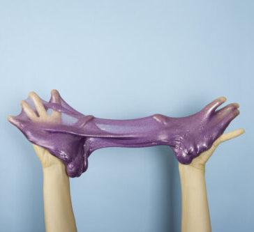 Close up on shiny purple or violet slime in the hand isolated on blue background. Fun and stress relief concept